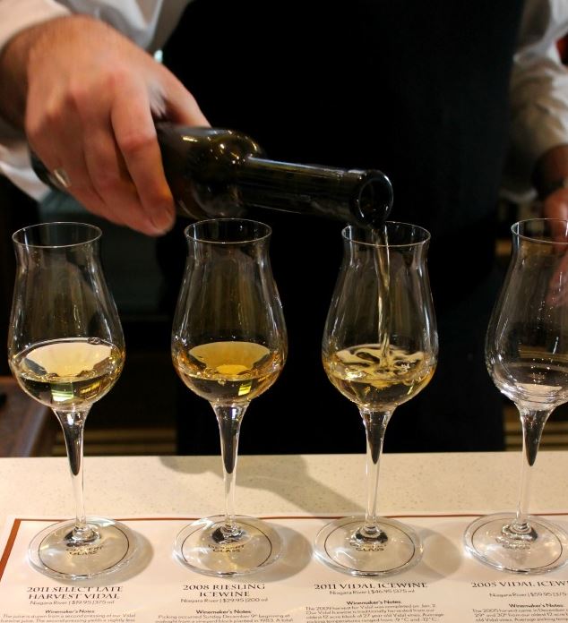 Four small, narrow tulip glasses holding small pours of icewine in a tasting flight, with a hand tipping the bottle