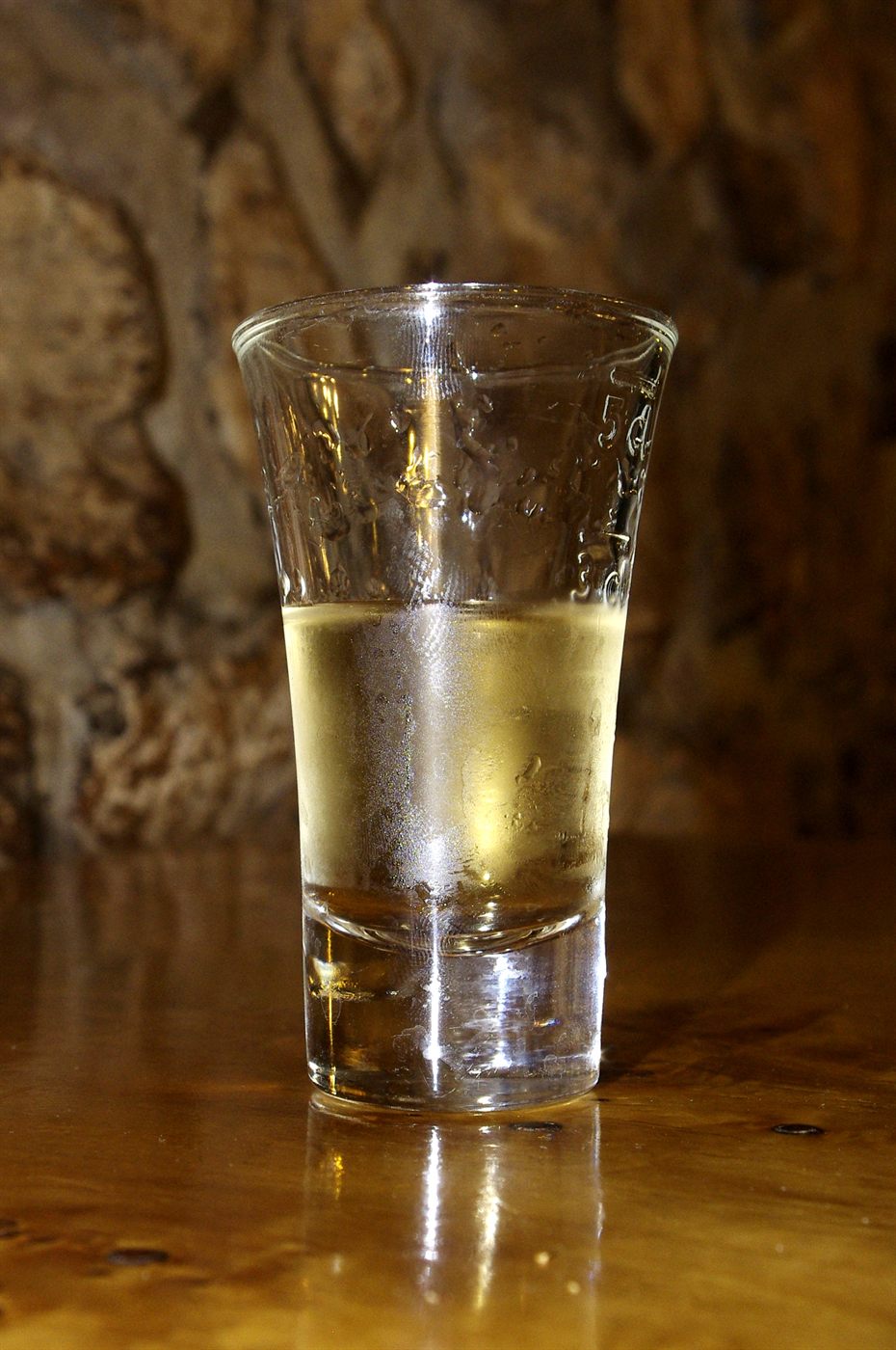 A traditional small pálinka glass, slightly flared at the top, holding apricot pálinka