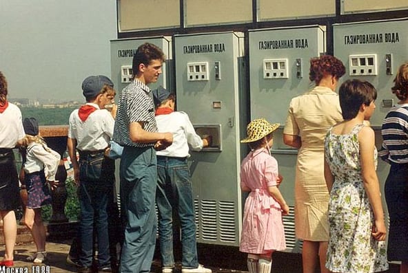 People gathered at a Soviet-era street soda machine — children in Pioneer scarves and adults