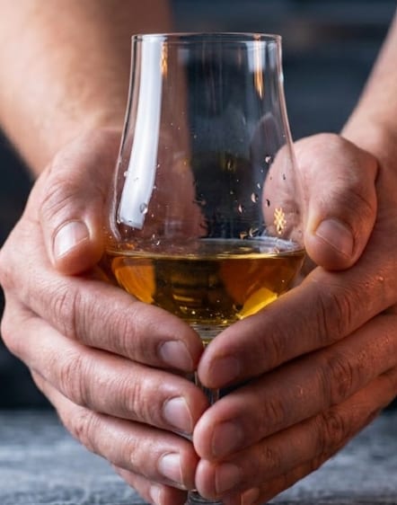 Cradling a whisky nosing glass in both hands to warm it